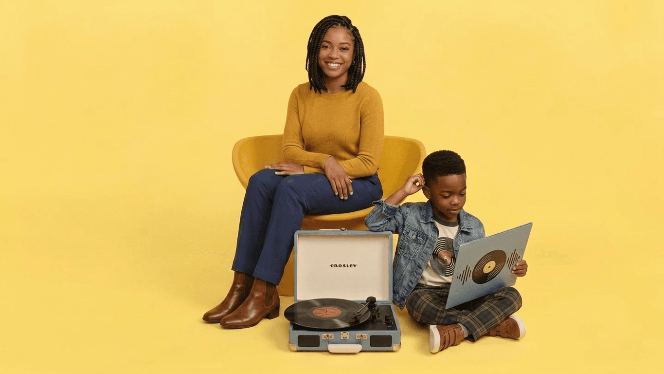 Female and child smiling while holding a vinyl cover, behind a record player