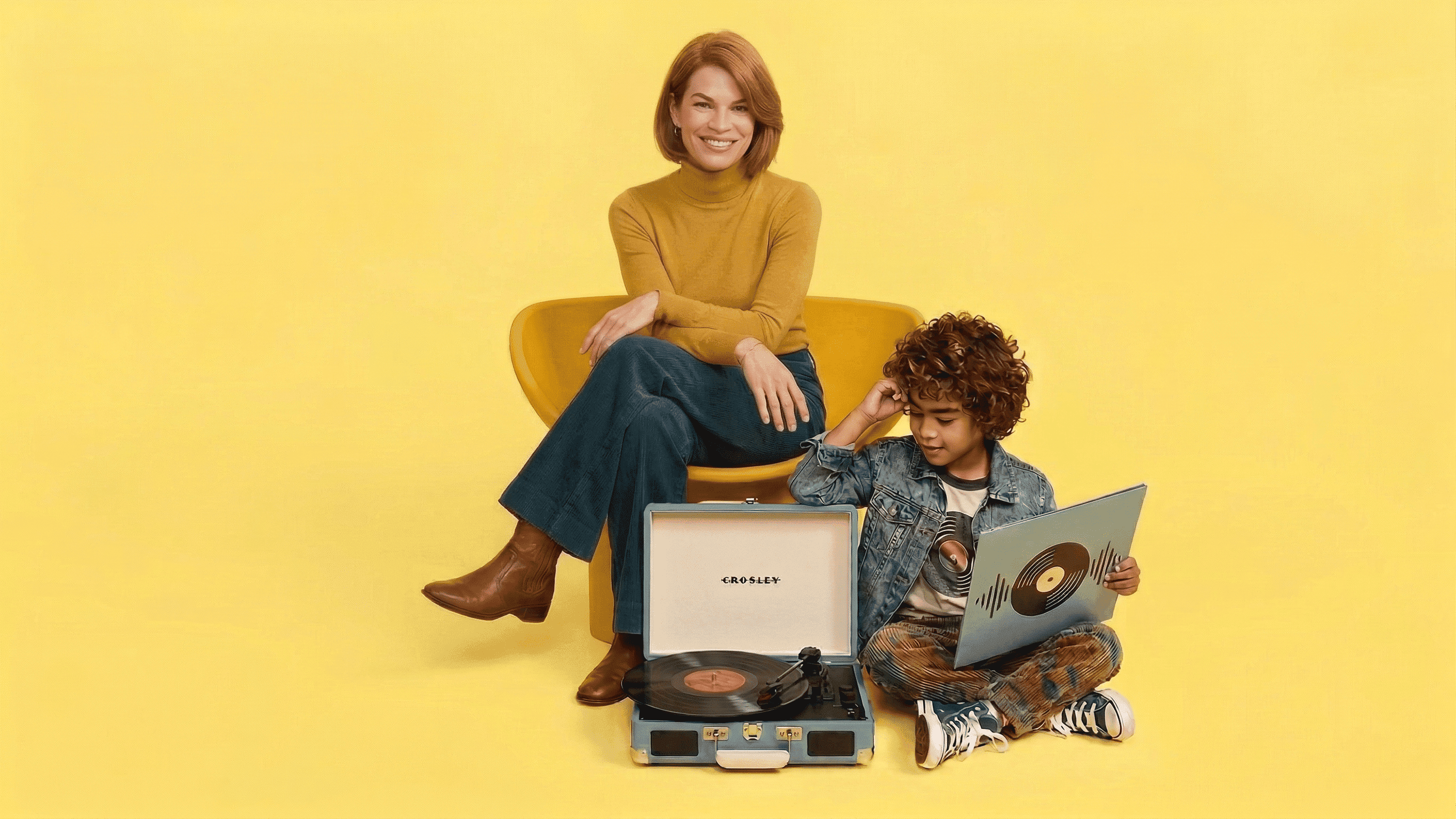 Female and child smiling while holding a vinyl cover, behind a record player